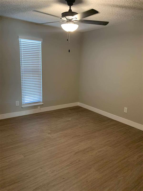 Empty room with light brown wood-look flooring, tan walls, a window with blinds, and a ceiling fan.