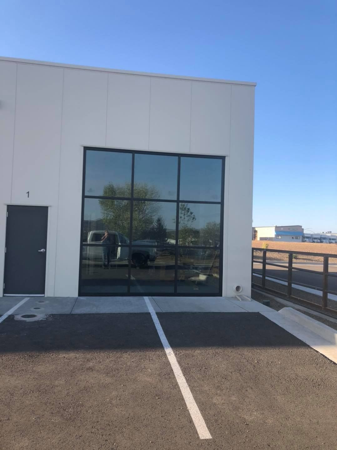 Exterior of a white building with large black-framed windows, a black door, and parking lines on asphalt.