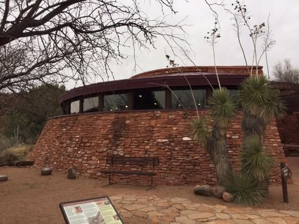 Red brick circular building with windows, bench, and desert plants.