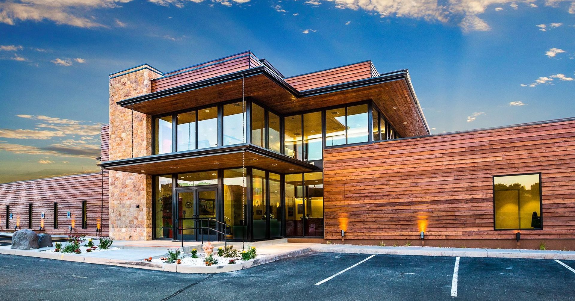 Modern building with stone and wood exterior, large windows, blue sky.