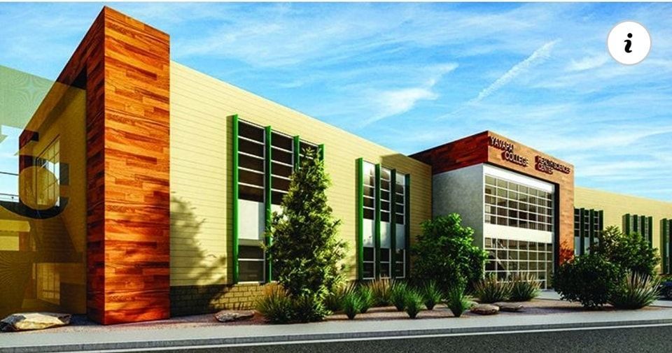 School building with tan and wood facade, green window frames, and landscaping under a blue sky.