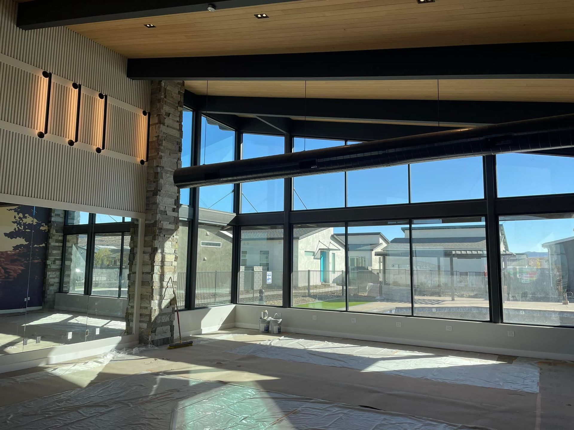 Interior view of a building under construction, featuring large windows and stone columns. Sunlight streams in.