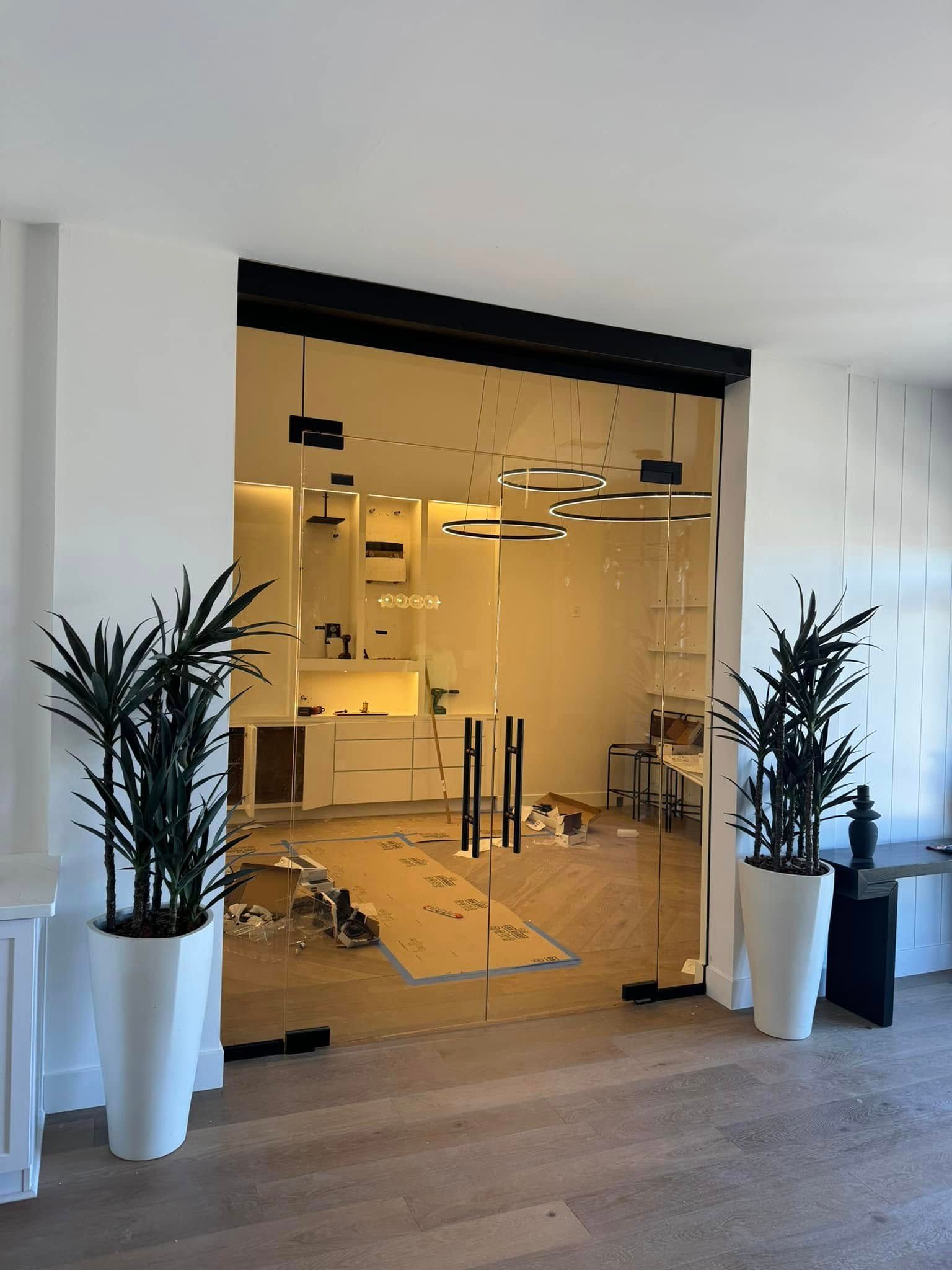 Glass doors open to a well-lit interior. Two potted plants flank the doorway.
