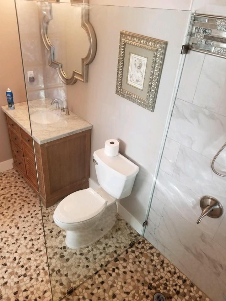Bathroom with a toilet, vanity, and shower. Tan pebble floor, light pink walls, and decorative mirror.