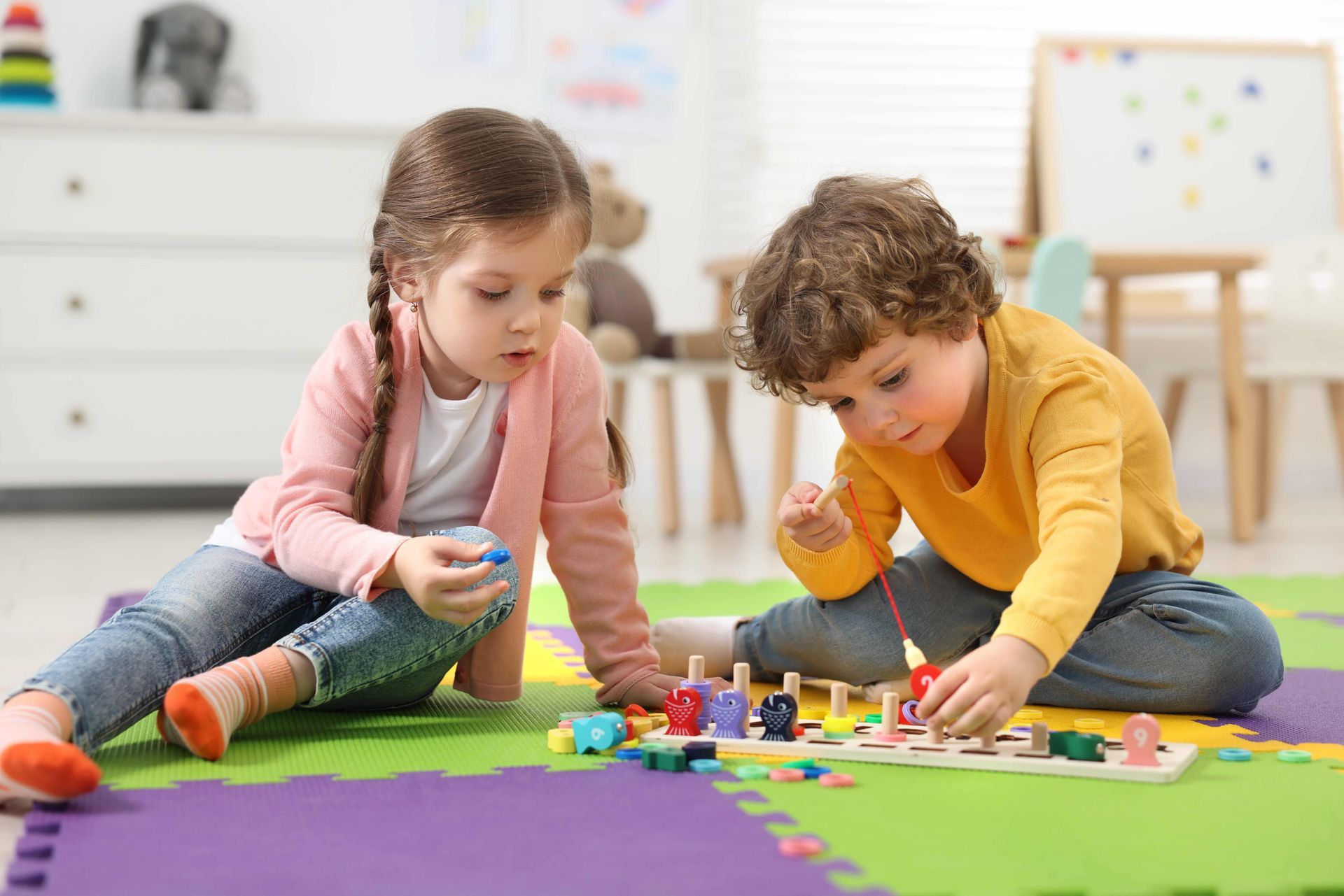 Two children playing with colorful wooden toys on a floor mat in a room.