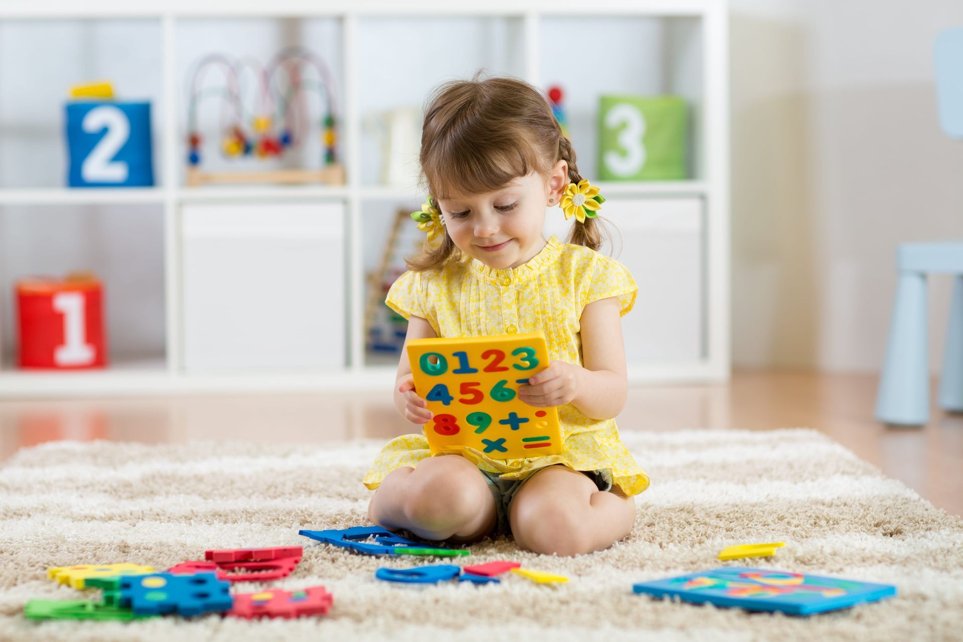 Girl sits on rug playing with colorful number puzzle in playroom.