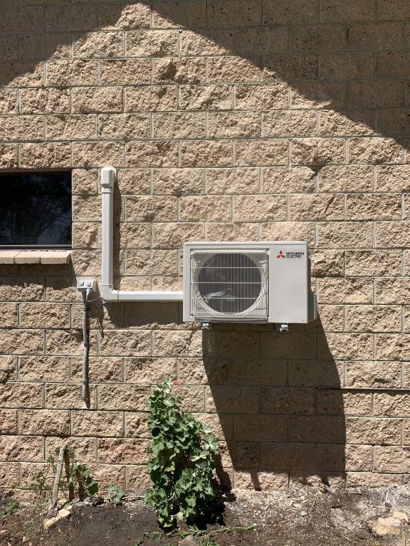 A White Air Conditioner is Mounted on the Side of a Brick Building — Condie Refrigeration & Air Conditioning In Murwillumbah, NSW