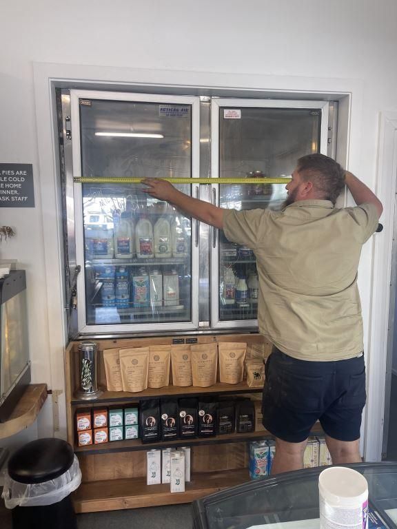 A Man is Measuring a Refrigerator Door With a Tape Measure — Condie Refrigeration & Air Conditioning In Tweed, NSW