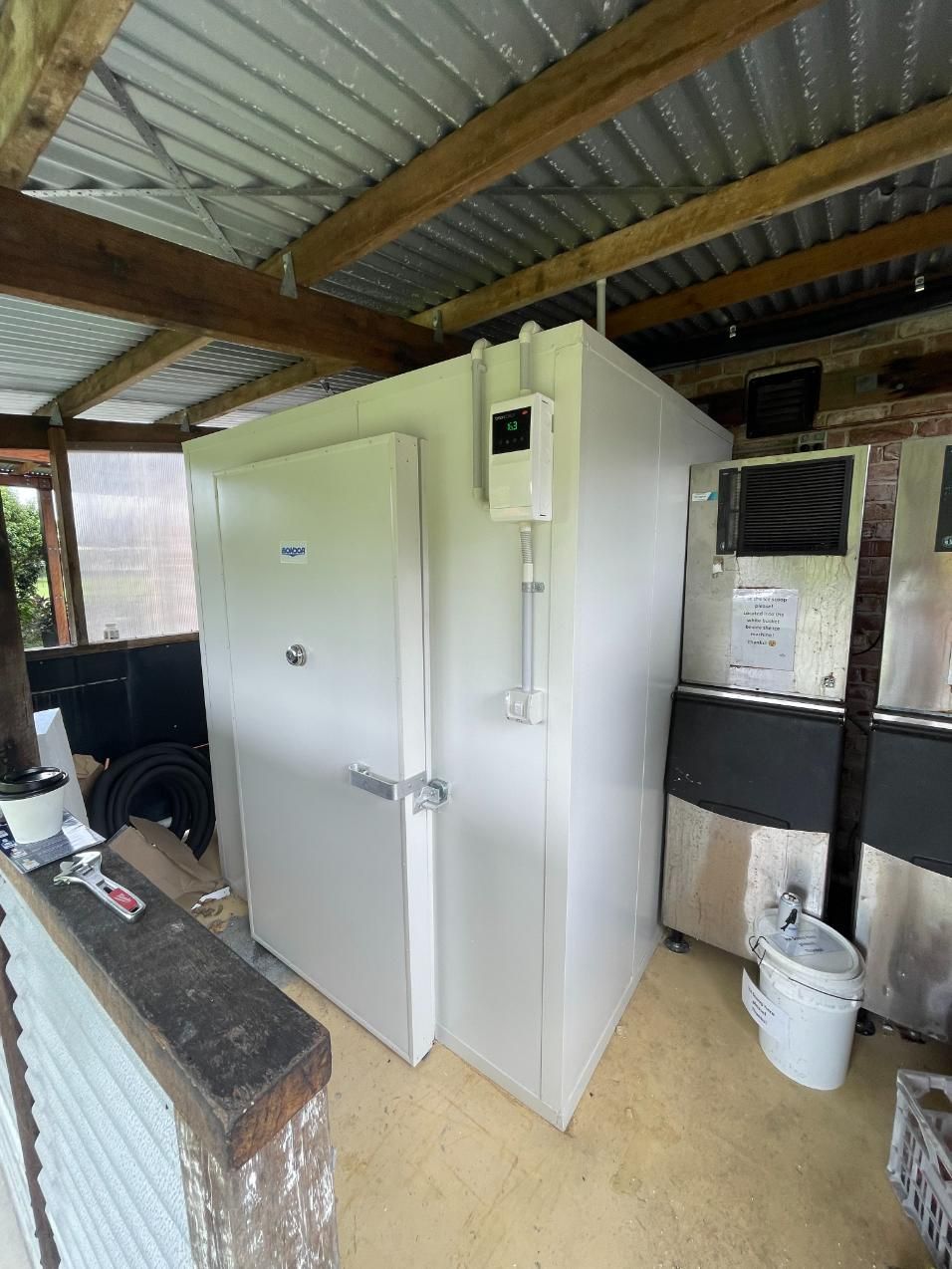 A Large White Refrigerator is Sitting Inside of a Shed — Condie Refrigeration & Air Conditioning In Pottsville, NSW
