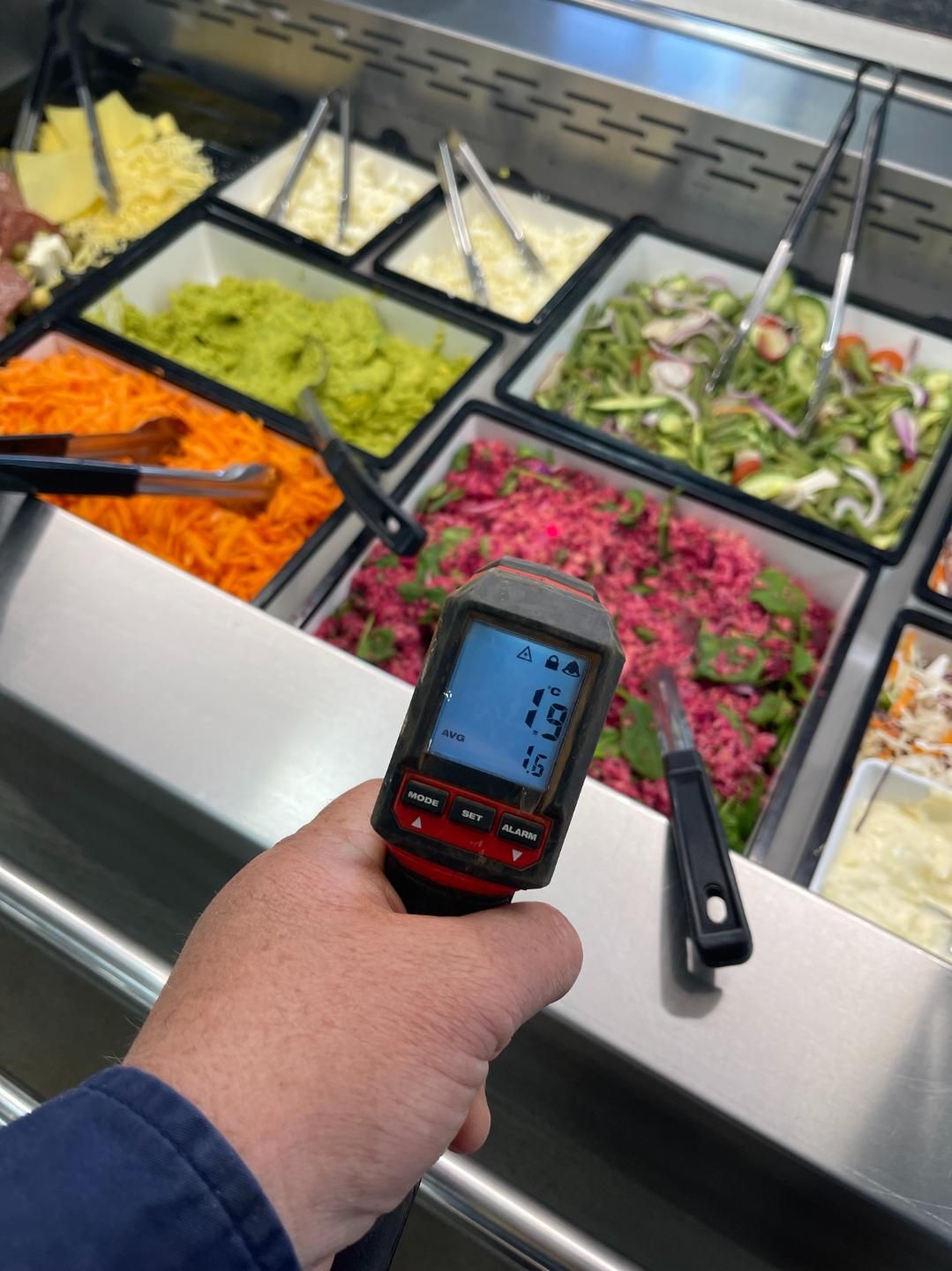 A Person is Holding a Thermometer in Front of a Salad Bar — Condie Refrigeration & Air Conditioning In Byron Bay, NSW