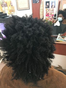 Close-up of a person with a natural afro hairstyle in a salon, with a stylist at the counter nearby.
