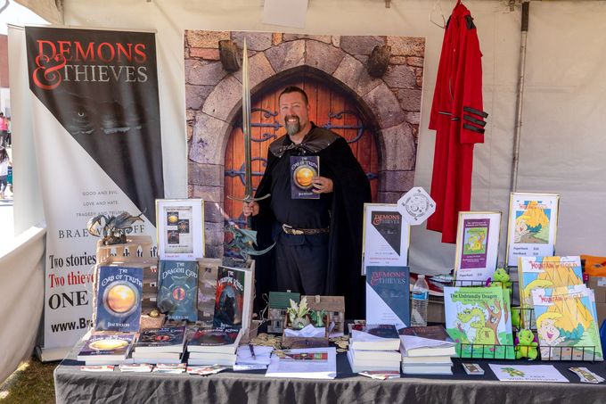 Author in costume holding a sword and promoting books. Text: Author booths.