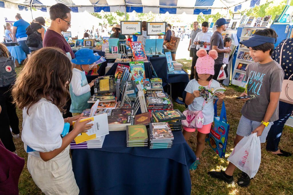 Children and adults looking at books for sale. Text: Books for kids, teens, and young adults
