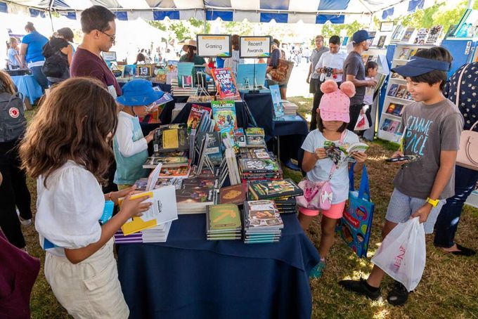 Children and adults looking at books for sale. Text: Books for kids, teens, and young adults.