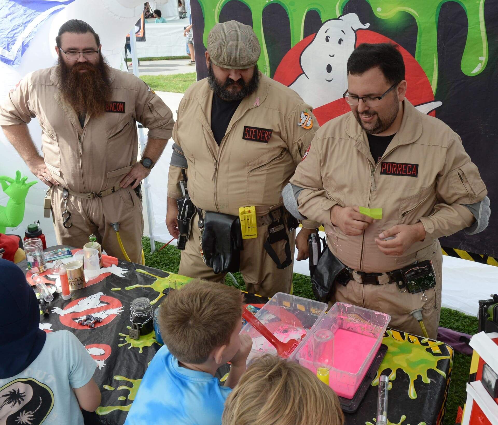 Three characters in Ghostbusters costumes interacting with young participants at an activity table.