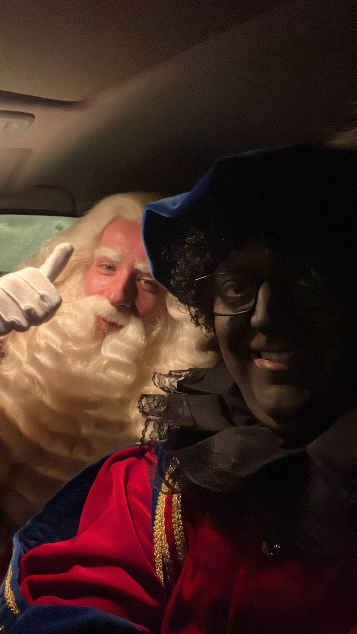 Twee mensen in feestelijke kostuums in een auto, de een verkleed 