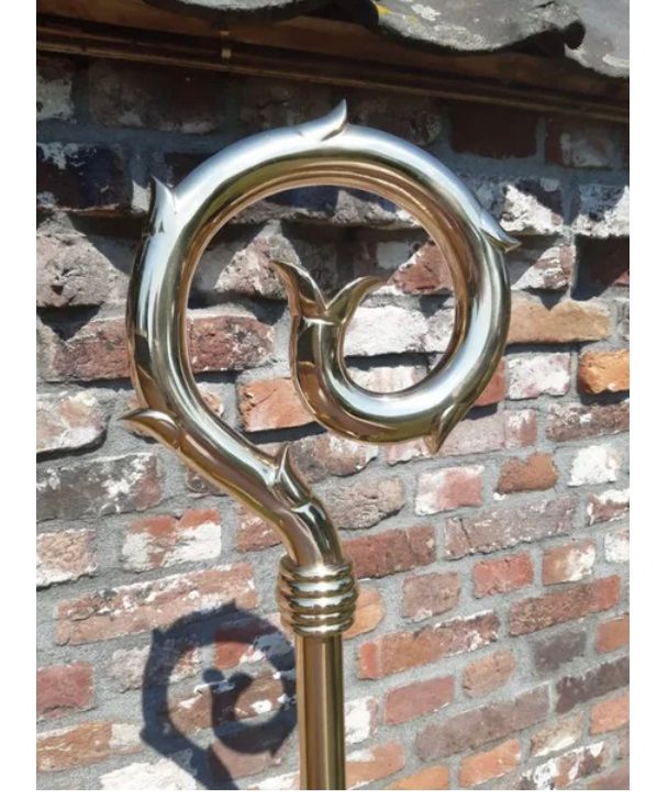 Glanzende messing decoratieve spiraalvormige bekroning gemonteerd op een bakstenen muur, met een gebogen schaduw eronder.