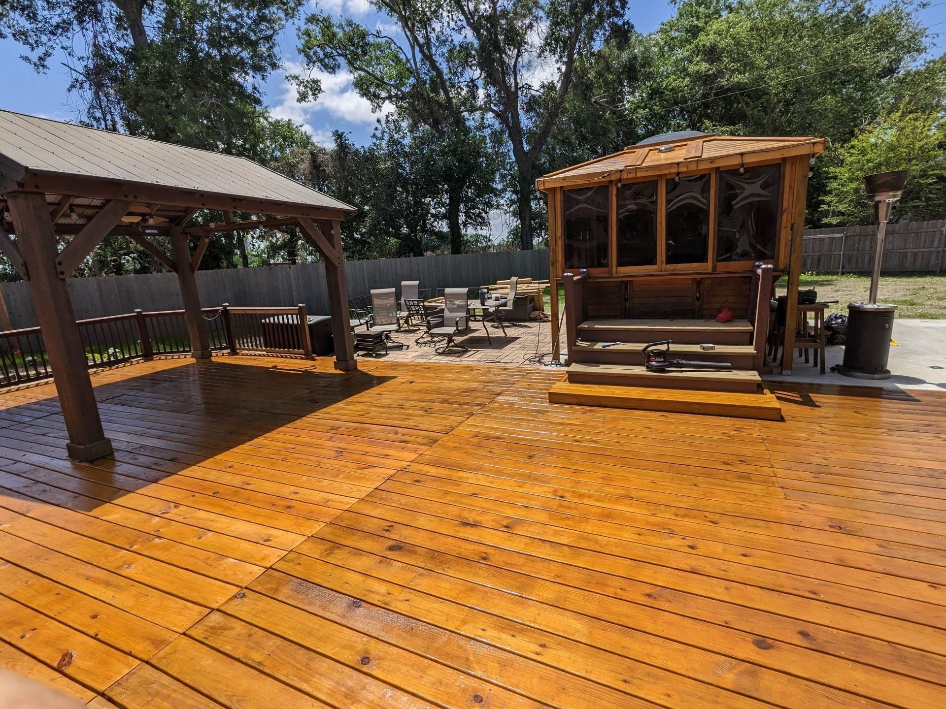 Wooden deck with two covered structures, seating, and fire pit in backyard.