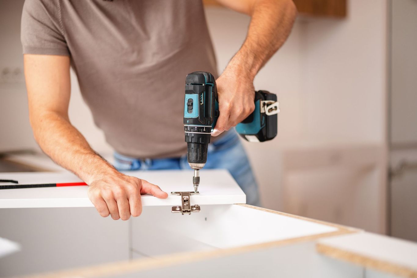 Person using a power drill to attach a hinge to a white cabinet.