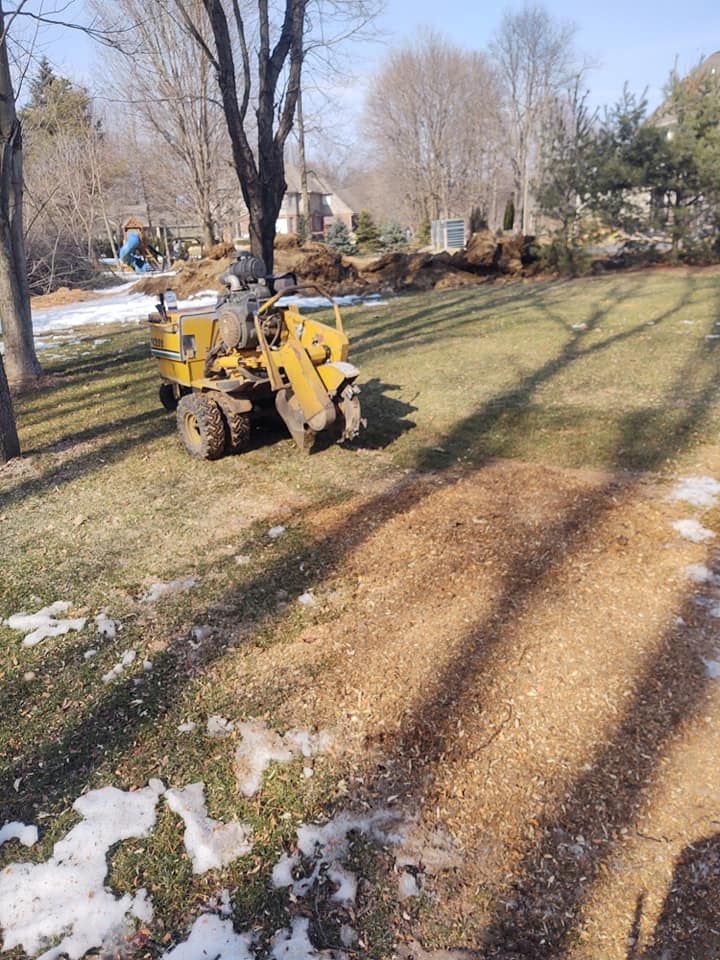 Tree stump grinding machine on grass, with wood chips and patches of snow.