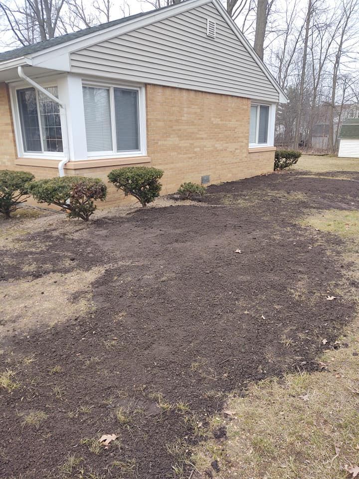 A house exterior with a patchy lawn and newly spread soil in the foreground.