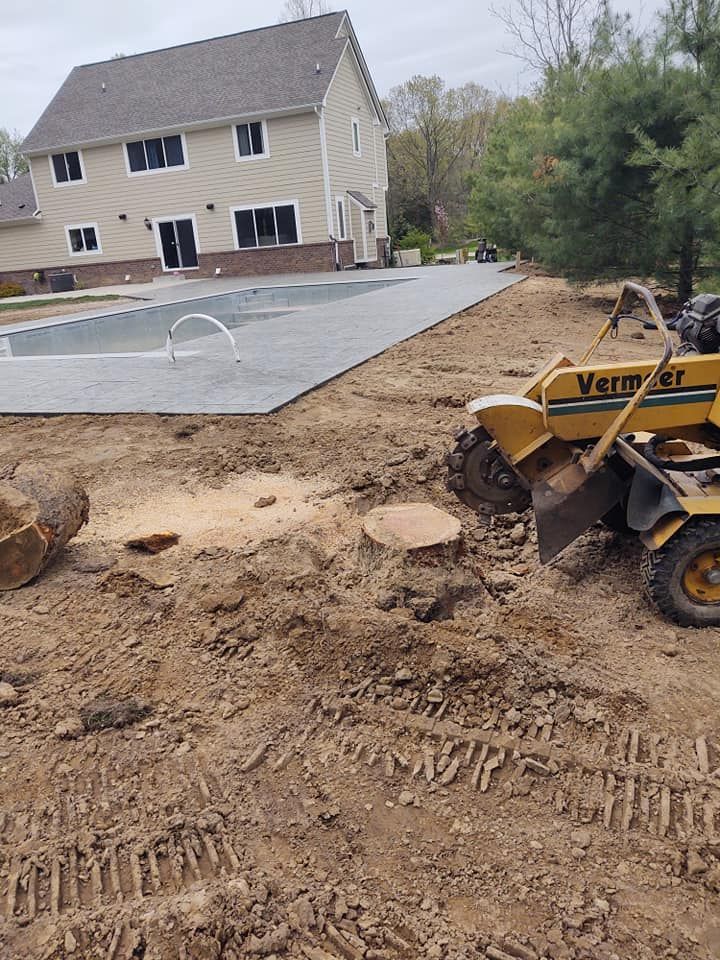 Stump grinder removing tree stump in a backyard, near a swimming pool and house, on a cloudy day.