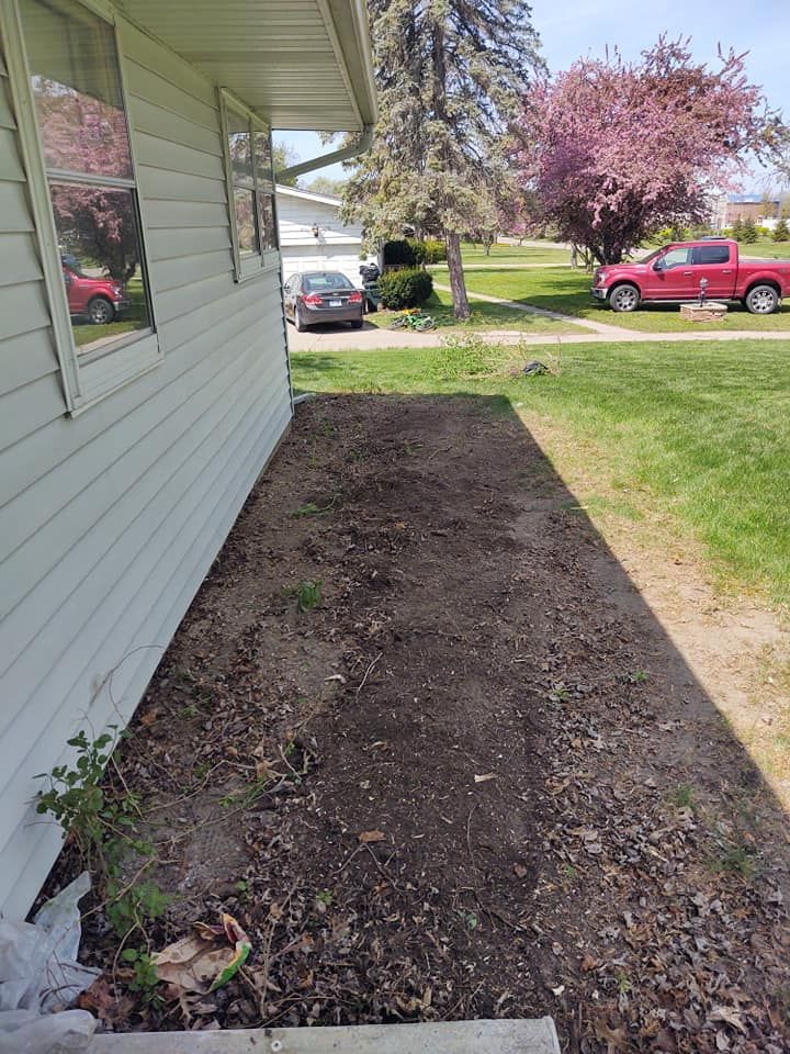 A narrow dirt patch alongside a white house. A red truck and car are visible in the background.