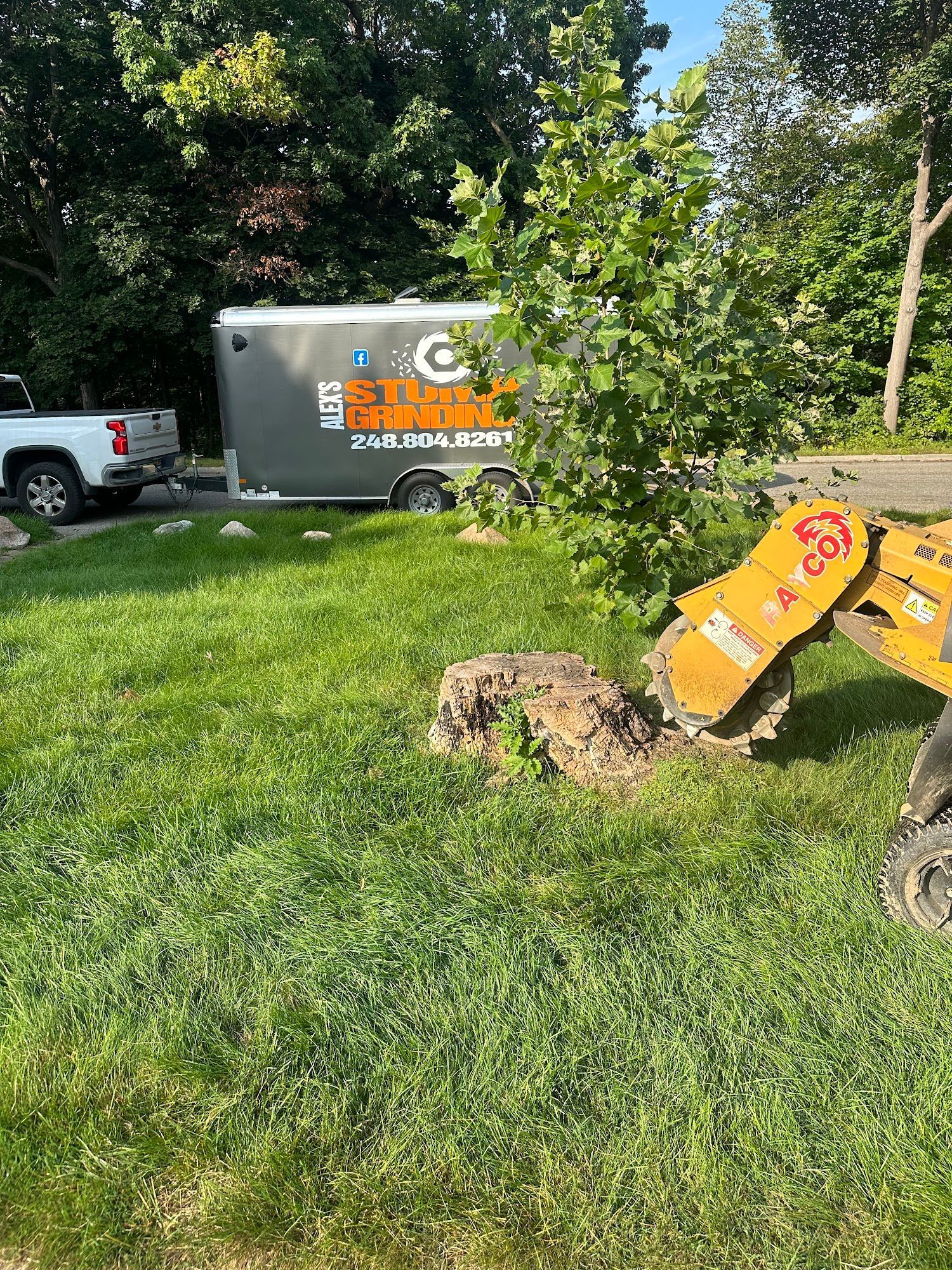 Yellow excavator digging in grass next to a trailer with 