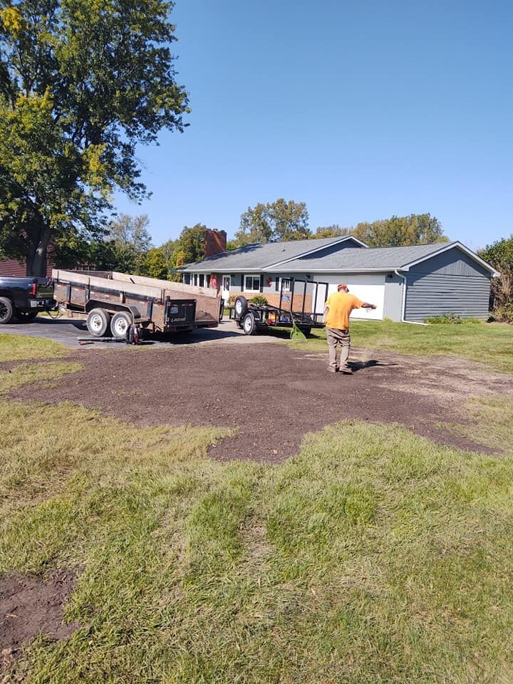 A person directs two trailers on a grass area in front of a house on a sunny day.