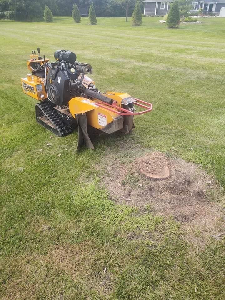 A stump grinder on tracks removes a tree stump on a grassy lawn.