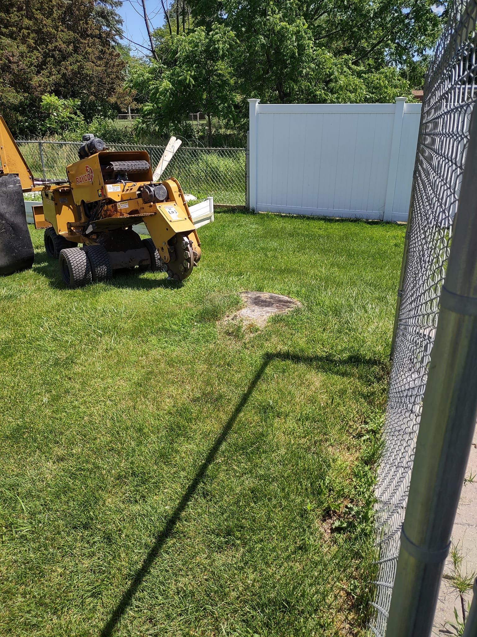 Stump grinder next to a tree stump on a lawn, next to a white fence.