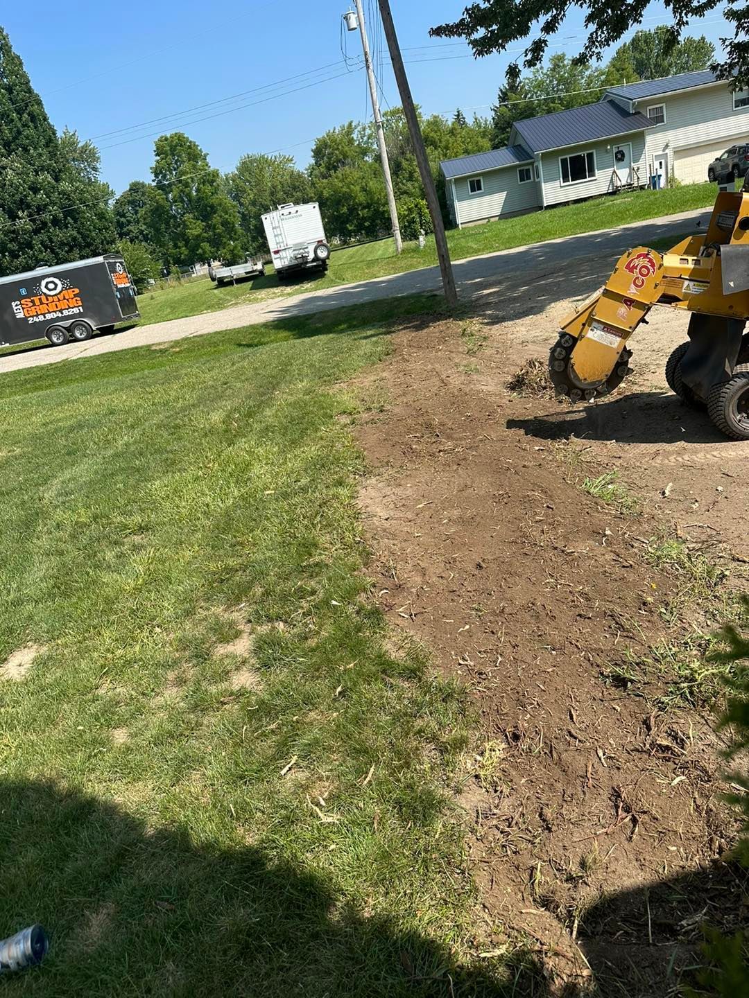 A stump grinder removing a tree stump on a residential lawn, sunny day.