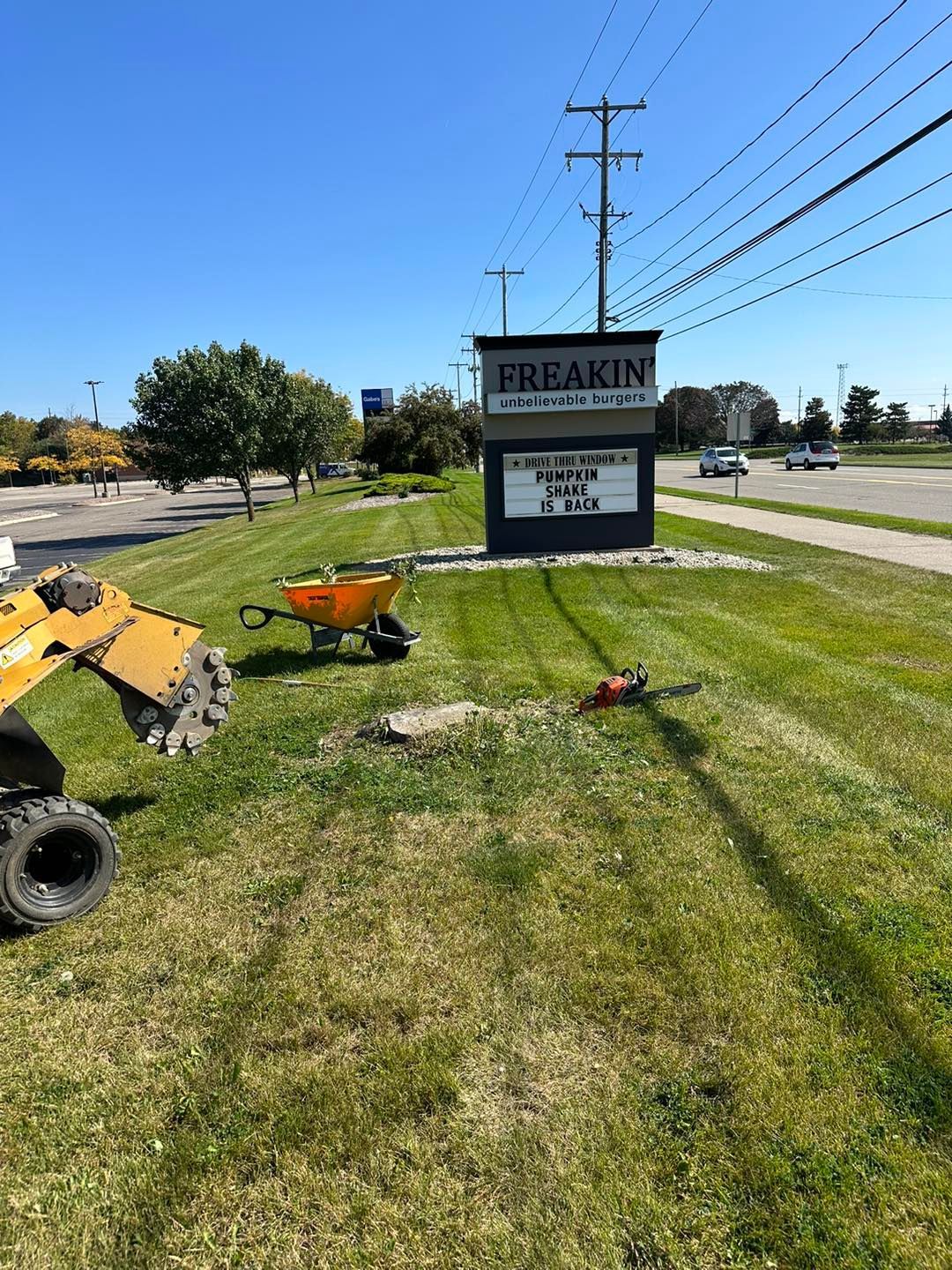 A stump grinder working on a grassy area near a sign for 