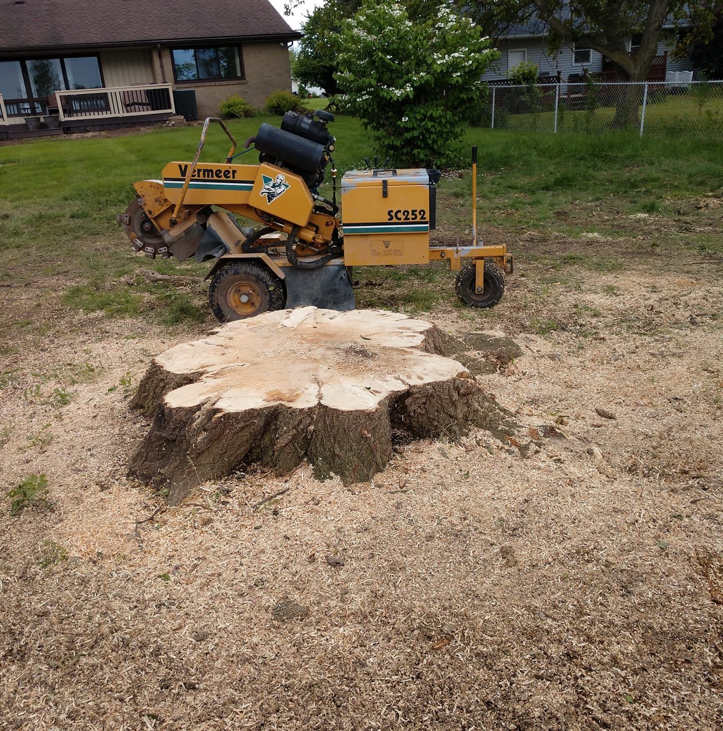 A yellow stump grinder next to a freshly ground tree stump on a grassy lawn.