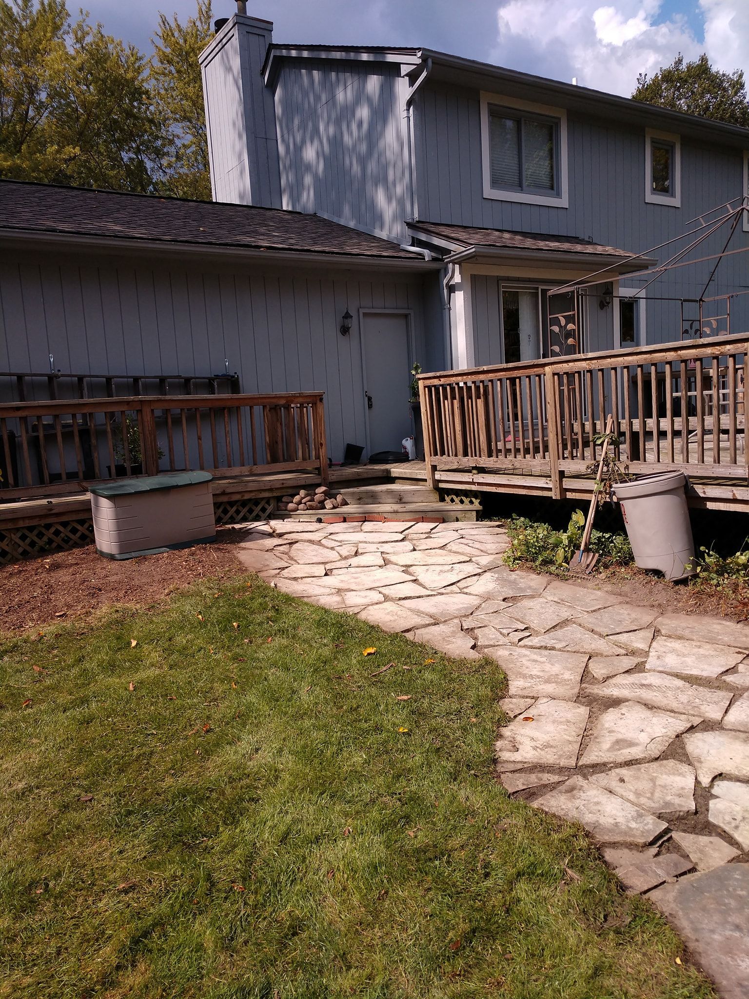 Backyard with stone path, wooden deck, gray house, and green grass.