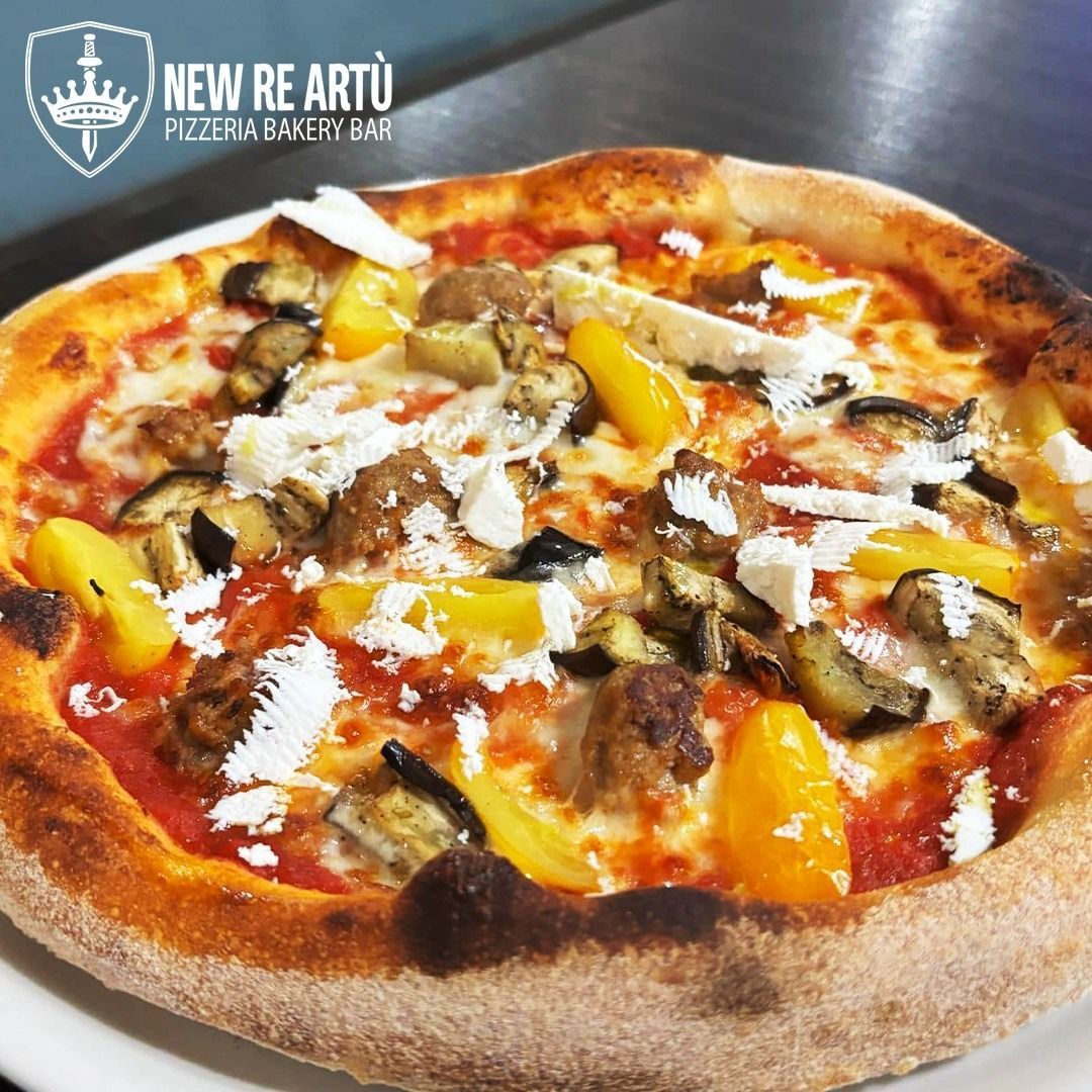 Una pizza cotta nel forno a legna condita con salsa di pomodoro, peperoni gialli, melanzane arrostite, salsiccia e formaggio bianco sbriciolato.