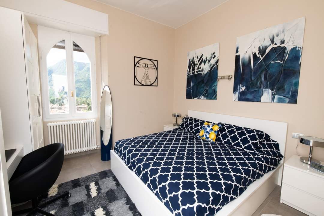Bedroom with a white bed, navy and white patterned bedding, art, and a view through a window.