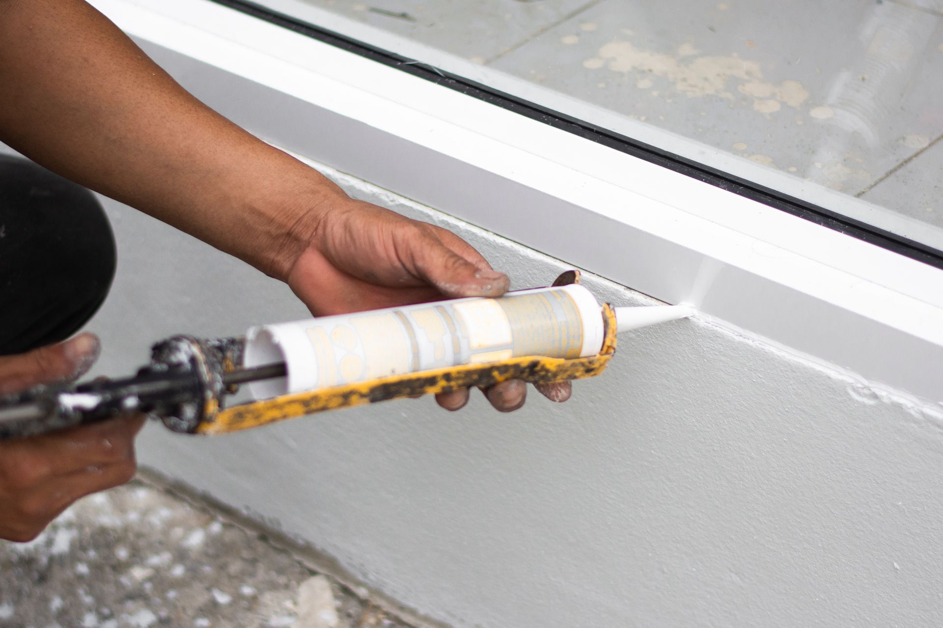 A person is applying caulk to a window sill.