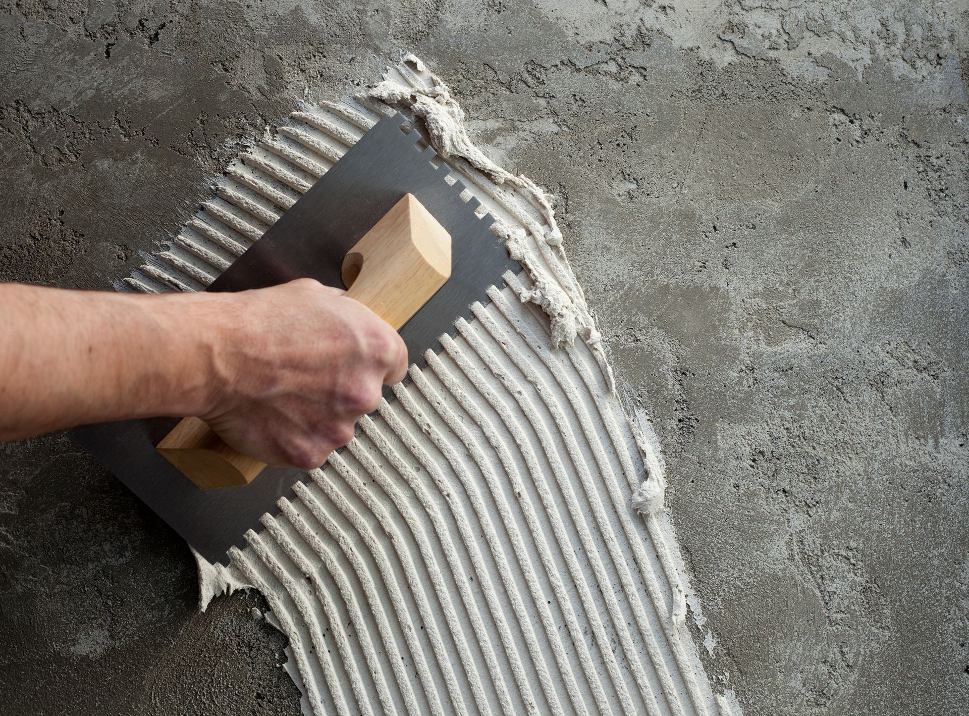 A person is spreading adhesive on a tile floor with a trowel.