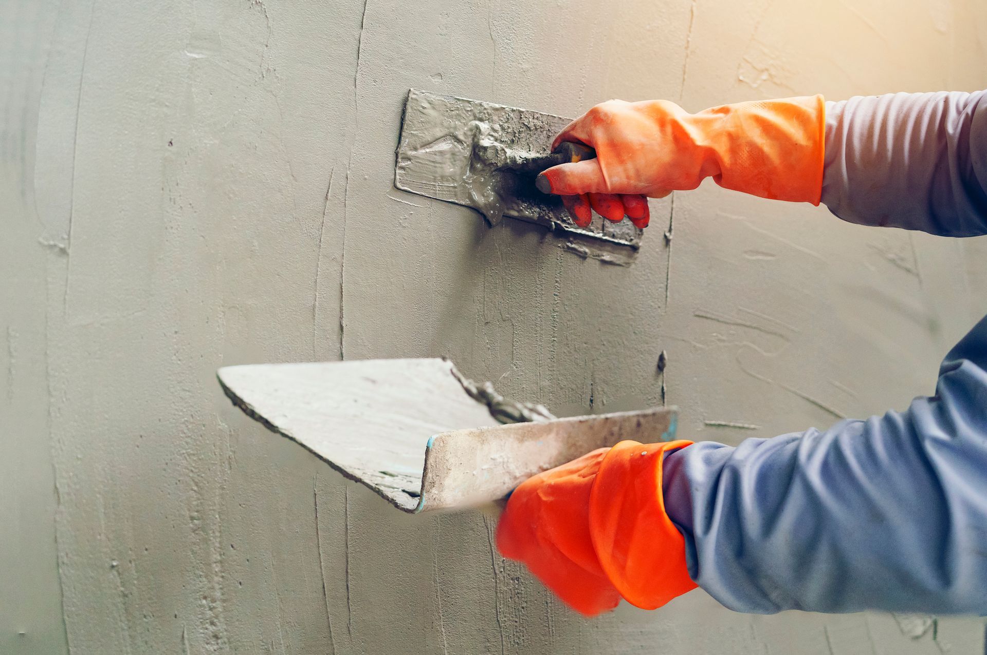 A person is plastering a wall with a trowel.