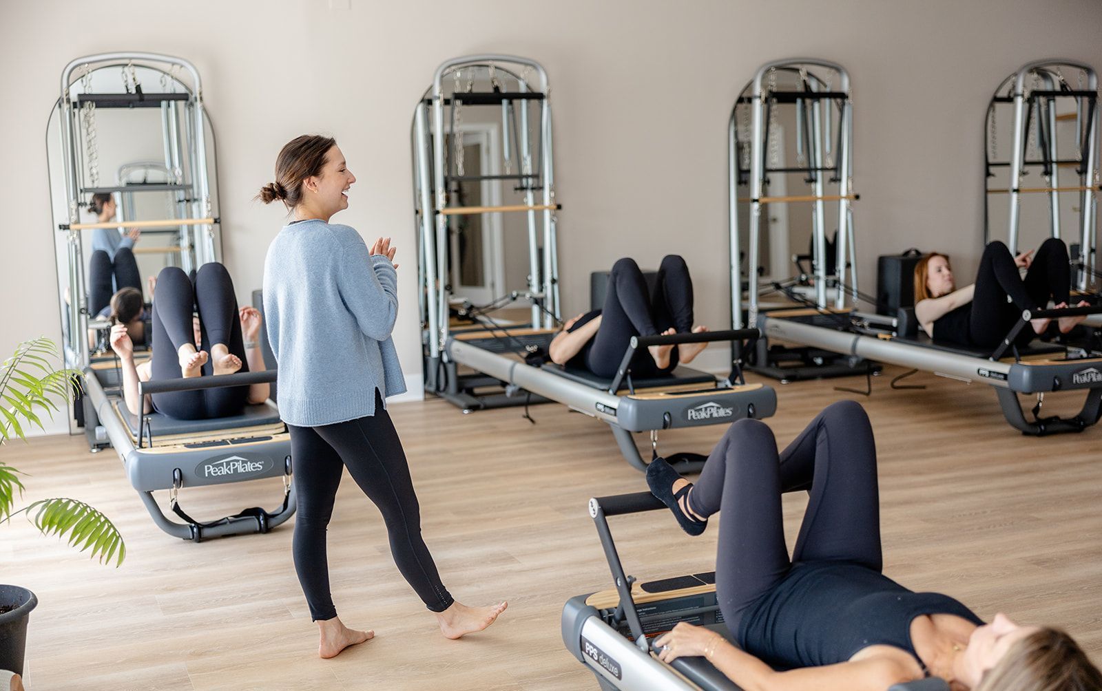 Pilates instructor leading class to find alignment using reformers in a bright studio.