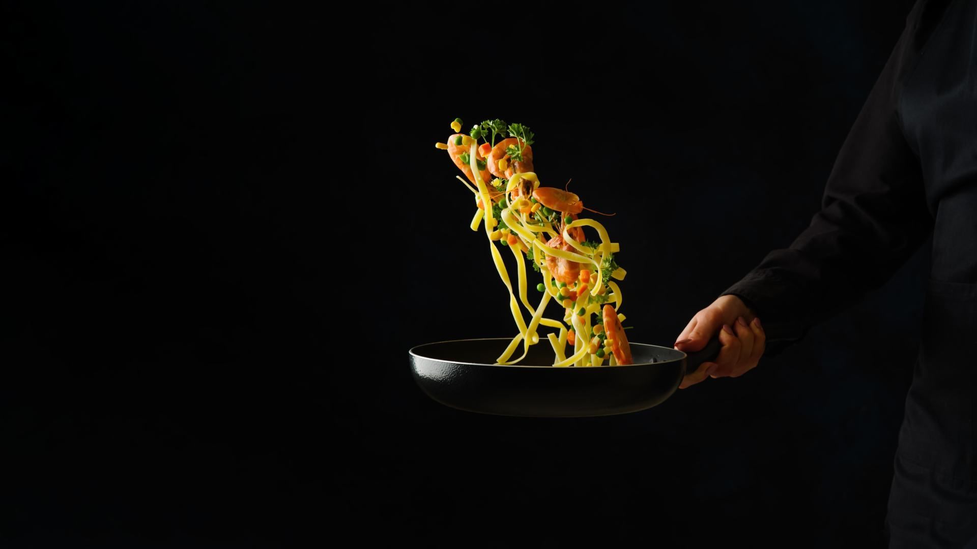 tossing pasta in a pan