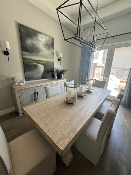 Elegant dining room with a long wood table, upholstered chairs, and a large painting on the wall.