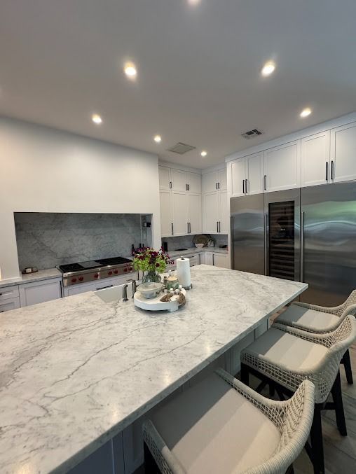 Modern white kitchen with a large island, stainless steel appliances, and marble countertops.