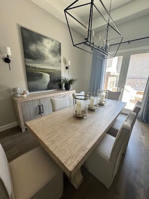 Elegant dining room with light-colored wood furniture, large painting, and chandelier, overlooking a cityscape.