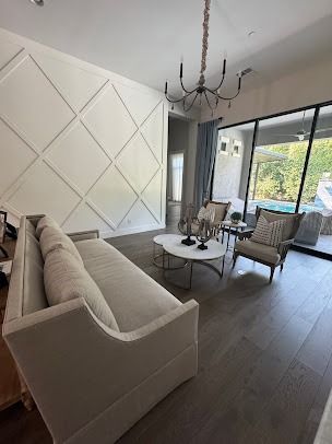 Living room with diamond wall design, beige sofa, armchairs, marble coffee table, dark floors, and pool view.