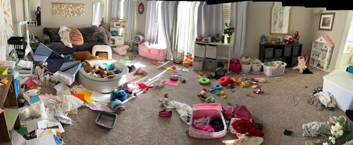 A living room with scattered toys and furniture. The setting is messy with lots of colors and objects on the floor.