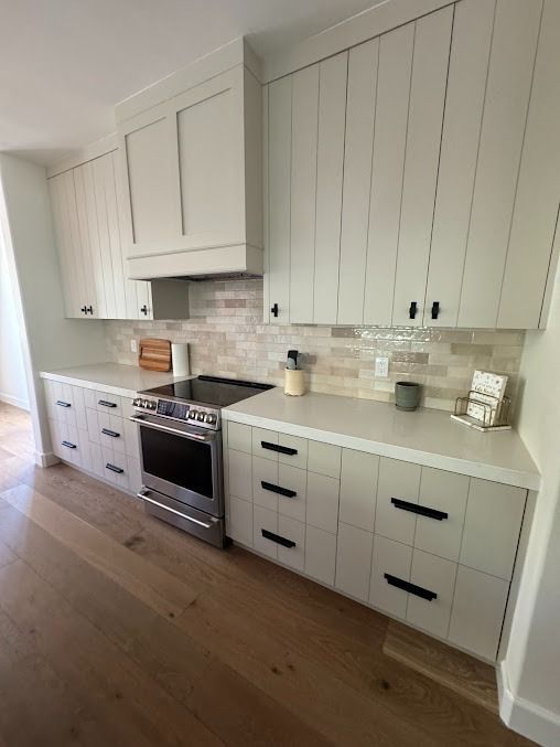 Modern kitchen with light cabinets, stainless steel range, white countertops, and wood flooring.