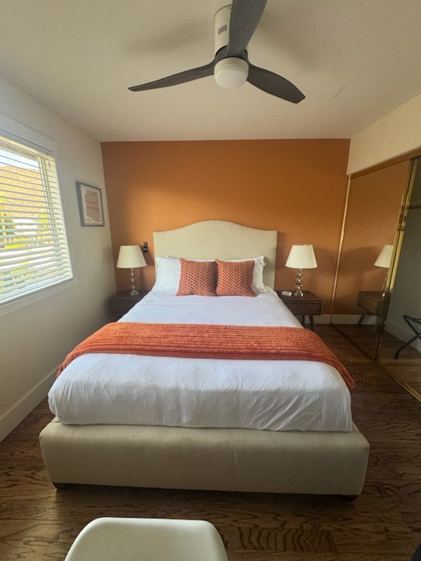 Bedroom with orange accent wall, bed, nightstands, ceiling fan, and window.