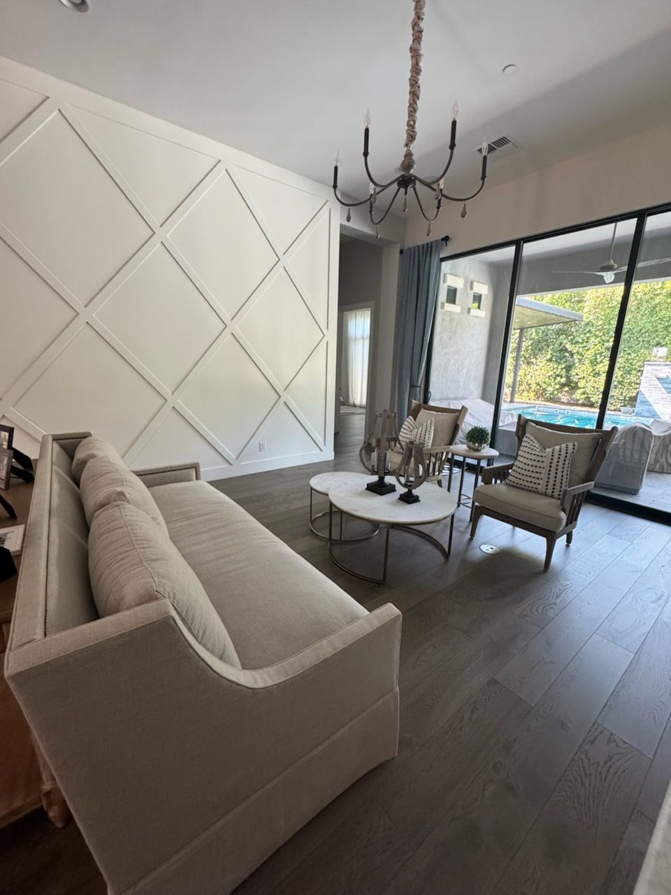 Living room with geometric accent wall, beige sofa, chairs, and round coffee table. Patio in background.